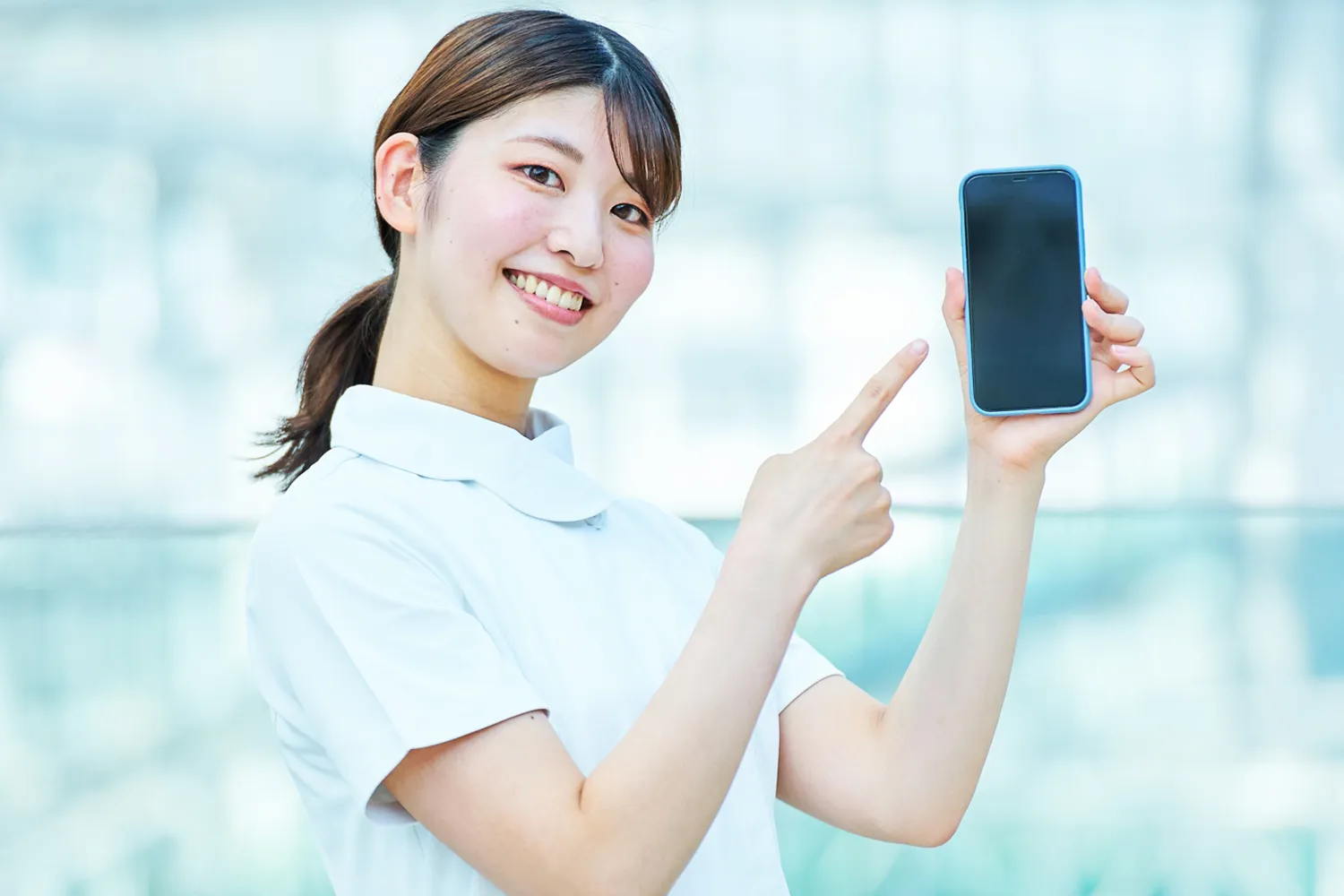 笑顔でスマートフォンを示す看護師の写真